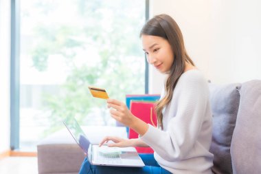 Güzel bir Asyalı kadının portresi evde online alışveriş için dizüstü bilgisayar kartı kullanıyor.