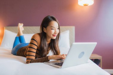 Asyalı güzel bir kadının portresi yatak odasının iç kısmında kredi kartıyla birlikte dizüstü bilgisayar kullanıyor.