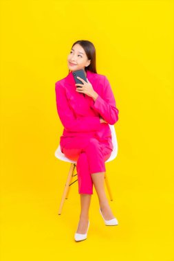 Güzel bir Asyalı kadın portresi sarı renkli izole edilmiş arka planda akıllı cep telefonu kullanır.