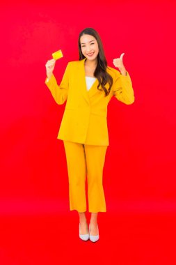 Güzel bir Asyalı kadının portresi kırmızı arka planda kredi kartıyla cep telefonu kullanıyor.