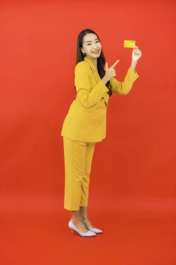 Güzel bir Asyalı kadının portresi kırmızı arka planda kredi kartıyla cep telefonu kullanıyor.