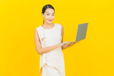 Asyalı güzel bir kadının portresi. Sarı izole edilmiş arka planda dizüstü bilgisayarla gülümsüyor.