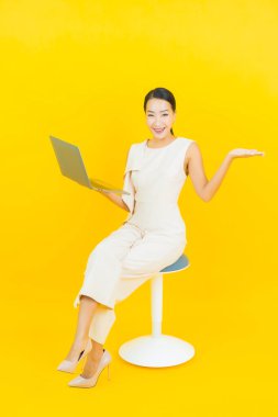 Asyalı güzel bir kadının portresi. Sarı izole edilmiş arka planda dizüstü bilgisayarla gülümsüyor.