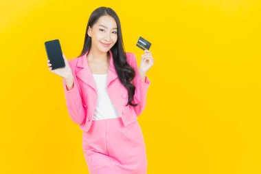 Asyalı güzel bir kadının portresi sarı arka planda akıllı cep telefonuyla gülümsüyor.