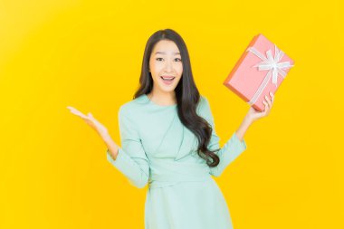 Güzel bir Asyalı kadının portresi. Arka planda kırmızı hediye kutusuyla gülümsüyor.