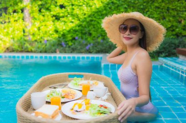 Genç Asyalı kadının portresi mutlu bir gülümseme ile otel havuzunda yüzen kahvaltı tepsisinin keyfini çıkar.