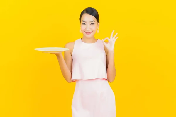亚洲年轻貌美的女子面带微笑 带着黄色底色的空盘子 — 图库照片