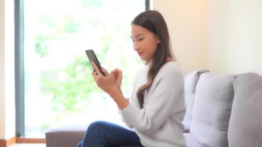 Güzel Asyalı kadının evde akıllı telefon kullandığının görüntüleri.