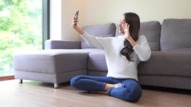 Evdeki kanepede akıllı telefon kullanan güzel bir Asyalı kadının görüntüsü.
