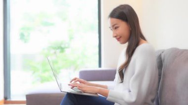 Evdeki kanepede dizüstü bilgisayarla çalışan güzel bir Asyalı kadının görüntüleri.