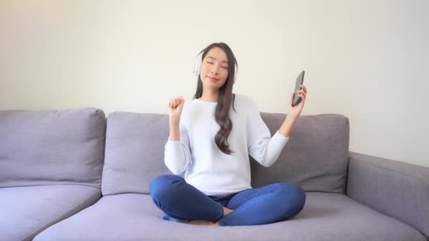 Metraje Hermosa Mujer Asiática Escuchando Música Con Auriculares Sofá Casa — Vídeo de stock