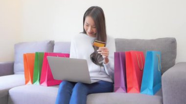 Güzel Asyalı kadının evdeki kanepede dizüstü bilgisayarla e-alışveriş yaptığı görüntüler.