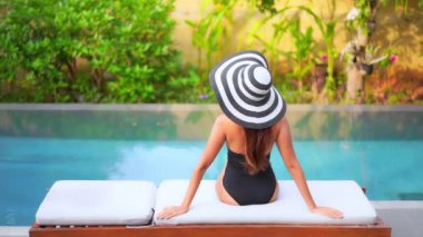 Güzel bir Asyalı kadın portresi tatil köyünde yüzme havuzunda rahatlıyor.