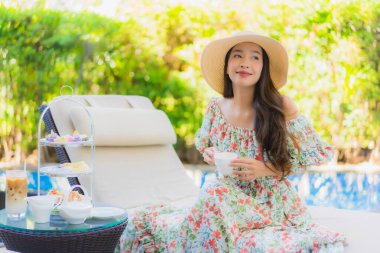 Güzel bir portre genç Asyalı kadın, ikindi çayıyla kahve setiyle oteldeki havuzda sandalyede oturuyor.