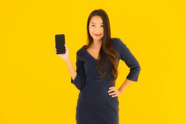 Akıllı cep telefonlu güzel Asyalı kadın portresi ya da sarı izole edilmiş arka planda cep telefonu.