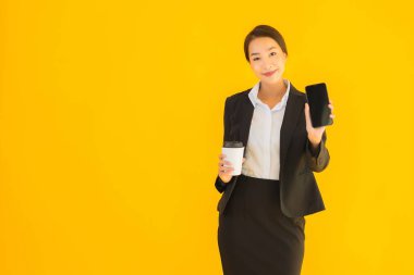 Portre güzel genç Asyalı kadın akıllı cep telefonu ve kahve fincanı ile izole edilmiş sarı arka planda