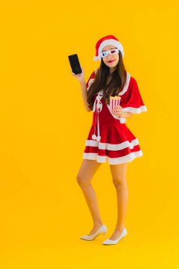 Güzel bir Asyalı kadın portresi patlamış mısır ve 3D gözlüklü noel şapkası takıyor sarı izole edilmiş arka planda film izlemeye hazır.