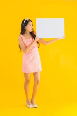 Güzel bir Asyalı kadın portresi sarı izole arkaplanda boş beyaz ilan panosu ve telif alanı gösteriyor.
