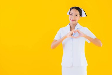 Güzel Asyalı genç Taylandlı hemşirenin portresi klinikteki ve hastanedeki hastalar için sarı izole edilmiş arka planda birçok eylem çalışmasında yer alıyor.