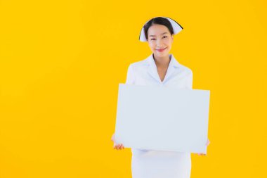Güzel bir Asyalı genç kadın portresi boş beyaz pano gösteriyor ve sarı izole edilmiş arka planda klinik ya da hastanede çalışıyor.
