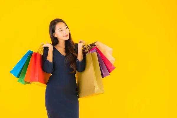 黄色の隔離された背景にカラフルなショッピングバッグを持つ肖像画の美しい若いアジアの女性 — ストック写真