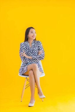 Güzel bir Asyalı kadın, sarı izole edilmiş arka planda hareketli bir şekilde sandalyede oturuyor.