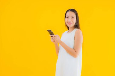 Sarı izole edilmiş arka planda akıllı cep telefonlu güzel Asyalı kadın portresi