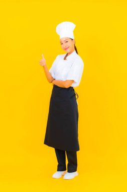 Güzel bir Asyalı kadın portresi ya da sarı izole arkaplanda şapkası olan aşçı üniforması.