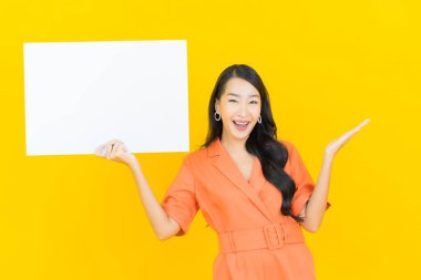 Asyalı güzel bir kadının portresi. Sarı arka planda boş beyaz ilan panosuyla gülümsüyor.