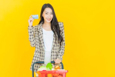 Renkli arka planda süpermarketten alınmış market sepetiyle gülümseyen güzel Asyalı kadın portresi.