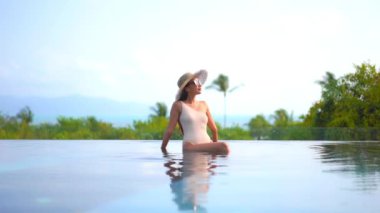 Güzel bir Asyalı kadın portresi tatil köyünde yüzme havuzunda rahatlıyor.