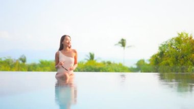 Güzel bir Asyalı kadın portresi tatil köyünde yüzme havuzunda rahatlıyor.