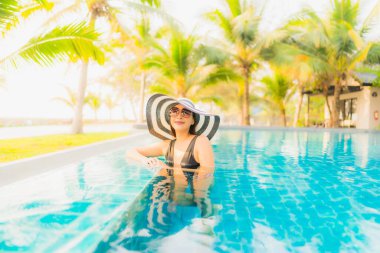 Güzel bir Asyalı kadın portresi, gün batımında palmiye ağacıyla birlikte havuz kenarında dinleniyor ya da tatil için gün doğumunda dinleniyor.