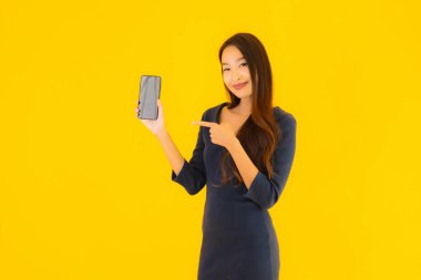 Akıllı cep telefonlu güzel Asyalı kadın portresi ya da sarı izole edilmiş arka planda cep telefonu.