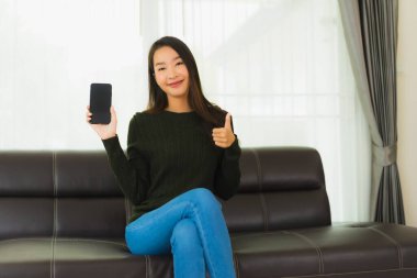 Güzel bir Asyalı kadın oturma odasındaki koltukta akıllı cep telefonu ya da cep telefonu kullanıyor.
