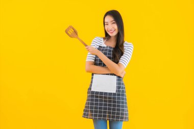Güzel bir Asyalı kadın portresi siyah tavalı önlük ve sarı izole arka planda Spatula giyer.