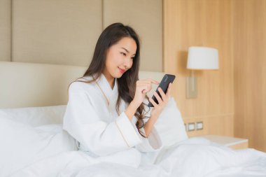 Yatak odasının içinde akıllı cep telefonlu güzel Asyalı kadın portresi.