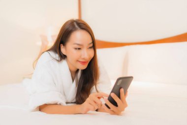 Güzel bir Asyalı kadın yatak odasının içinde akıllı cep telefonu kullanıyor.