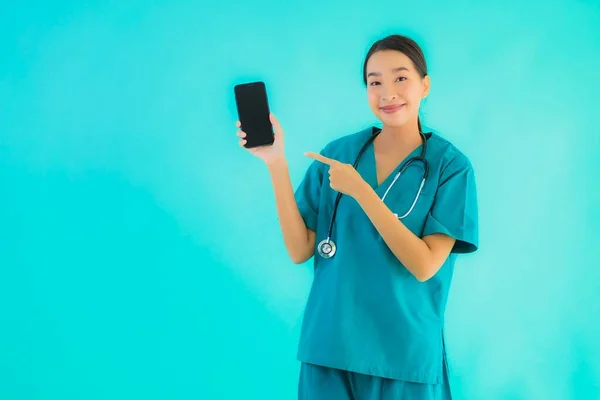 年轻美丽的亚裔女医生在蓝色孤立的背景下展示出聪明的手机 — 图库照片