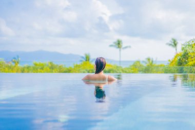 Güzel bir Asyalı kadın portresi gezide deniz manzaralı açık havuzda yüzüyor.