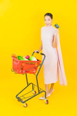 Sarı arka planda süpermarketten alınmış sepetli güzel Asyalı kadın portresi.