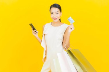 Sarı arka planda alışveriş çantasıyla gülümseyen güzel Asyalı kadın portresi
