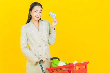 Renkli arka planda süpermarketten alınmış market sepetiyle gülümseyen güzel Asyalı kadın portresi.