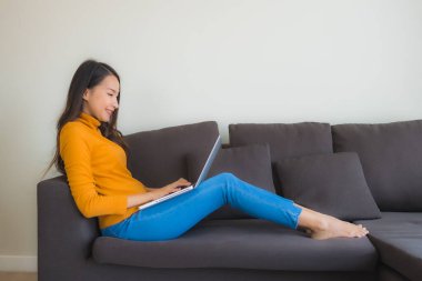 Genç Asyalı bir kadının oturma odasında çalışmak için dizüstü bilgisayar defteri kullanmasının portresi.