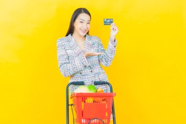 Renkli arka planda süpermarketten alınmış market sepetiyle gülümseyen güzel Asyalı kadın portresi.