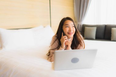 Yatak odasının iç kısmında dizüstü bilgisayarı ve cep telefonu olan güzel Asyalı kadın portresi.