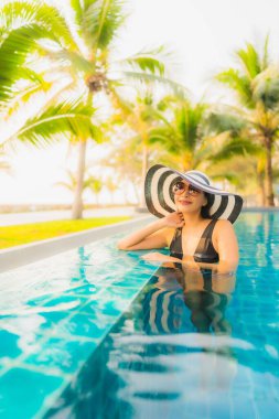 Güzel bir Asyalı kadın portresi, gün batımında palmiye ağacıyla birlikte havuz kenarında dinleniyor ya da tatil için gün doğumunda dinleniyor.