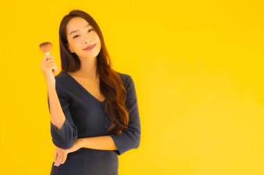 Sarı izole arkaplanda makyaj fırçası olan güzel bir Asyalı kadın portresi.