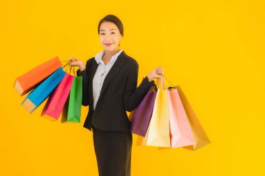 Sarı izole edilmiş arka planda alışveriş merkezinden alışveriş çantasıyla güzel bir genç Asyalı kadın portresi.
