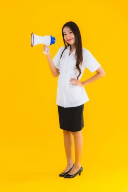 Güzel bir Asyalı genç doktor portresi. Sarı izole arka planda megafon kullanıyor.